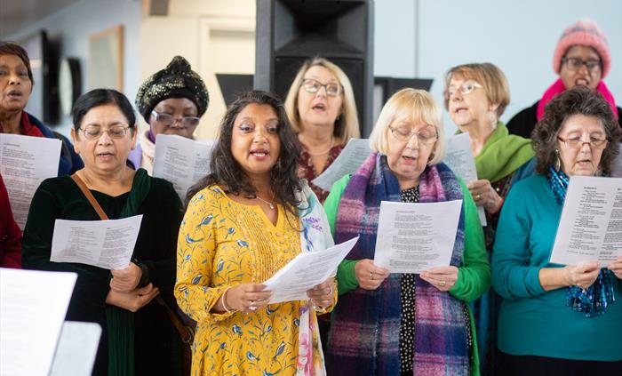 A group of women singing with song sheets.